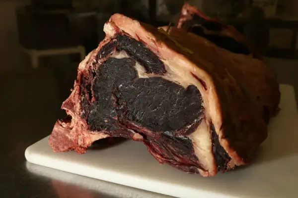 Gros morceau de viande maturée, prêt pour la cuisson. Sa couleur foncée et sa texture fibreuse promettent une saveur intense.
