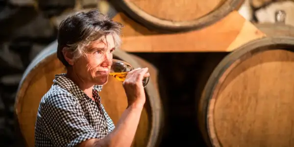 Une femme déguste un verre de vin de Pau, entourée de fûts de chêne dans une cave.