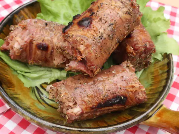 Trois andouillettes grillées au barbecue, servies sur un lit de laitue dans une assiette décorative.