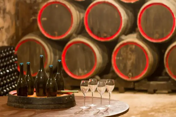 Bouteilles de champagne et verres sur un tonneau, prêts pour une visite de cave. Au fond, des fûts de chêne empilés.