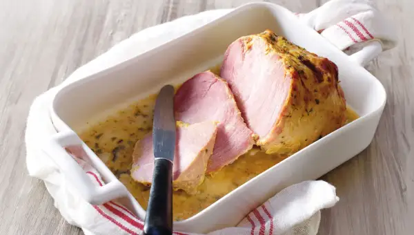Palette à la diable, tranchée et servie dans un plat blanc avec une sauce dorée. Un couteau est posé sur la viande.