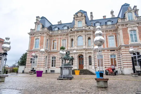 Devant un château, des sphères argentées, comme des habits de lumière, scintillent sur des structures métalliques, entourant une statue équestre.