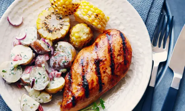 Un délicieux poulet grillé au sirop d'érable, servi avec une salade de pommes de terre crémeuse et des épis de maïs rôtis.