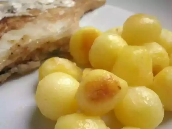 Une assiette de poisson grillé avec une généreuse portion de pomme de terre parisienne, dorée et appétissante.
