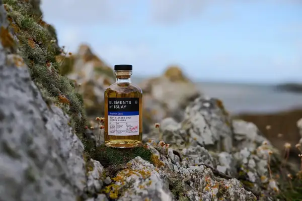 Bouteille de whisky "Elements of Islay" posée sur des rochers moussus, évoquant l'atmosphère sauvage de la distillerie Islay.