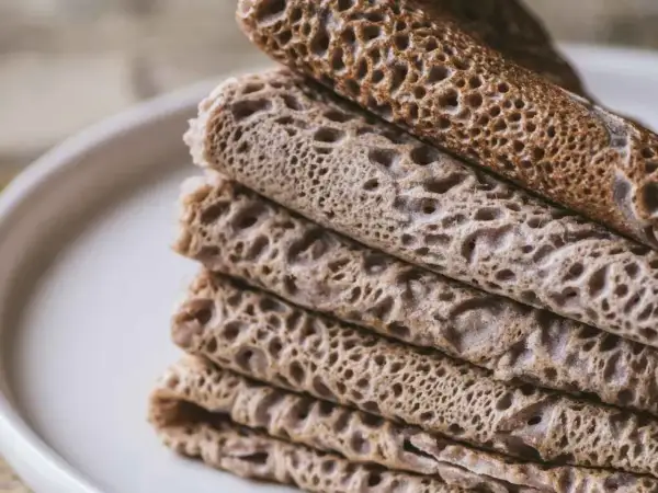 Pile de crêpes et de galettes, certaines roulées, d'autres pliées, avec une texture alvéolée. Un délice qui rappelle le goût de l'andouille.