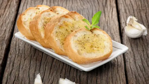 Tranches de pain grillé à l'ail, garnies d'herbes, rappelant la préfou recette traditionnelle. Une tête d'ail repose à côté.