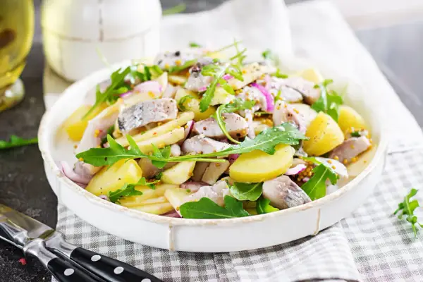 Salade de pommes de terre et hareng à l'huile, garnie de roquette et d'oignons rouges. Une recette simple et savoureuse.